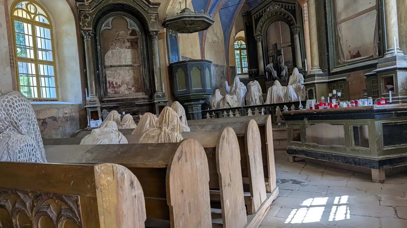 Innenansicht der Geisterkirche Lukova mit mehreren spitzenverhüllten Geisterfiguren in den Kirchenbänken
