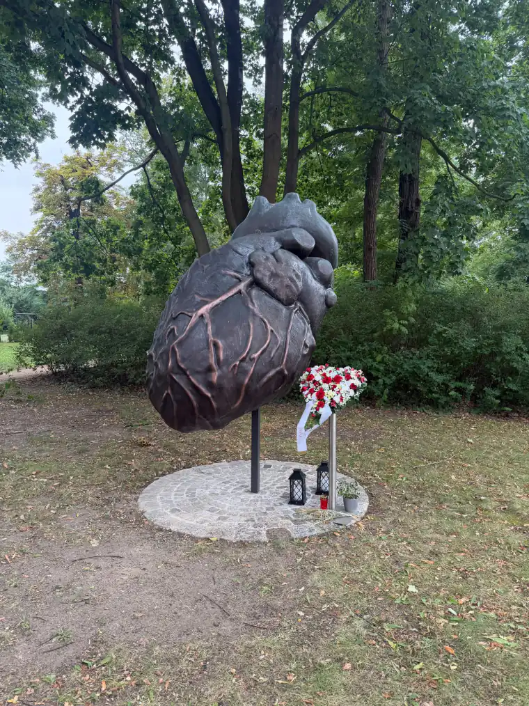 Bronzeskulptur eines anatomischen Herzens vor dem Plastinarium in Guben, davor niedergelegte Blumen, ein Kranz und Kerzen nach dem Tod von Gunther von Hagens