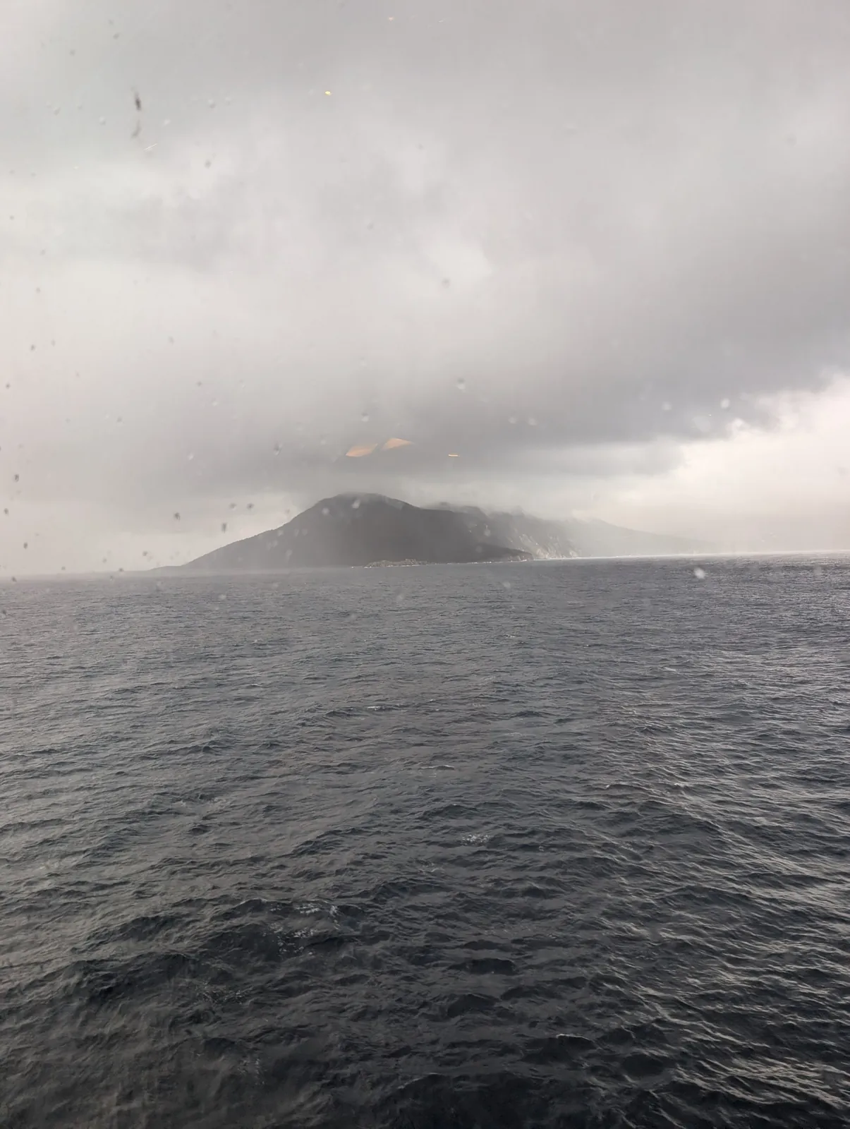 Wolkenverhangene Insel im Ionischen Meer, fotografiert durch ein regennasses Fenster der Fähre